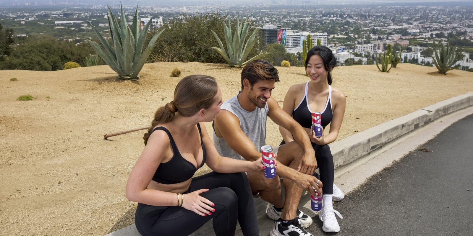 Three friends sitting outside with DATE cans, sweeping Hollywood Hills view